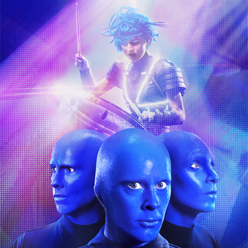 Vibrant promotional image featuring the Blue Man Group — three bald performers with bright blue-painted skin and expressionless faces — in the foreground. Behind them, a futuristic drummer with teal hair plays a large drum under dynamic, colorful lighting with purple, blue, and pink hues.